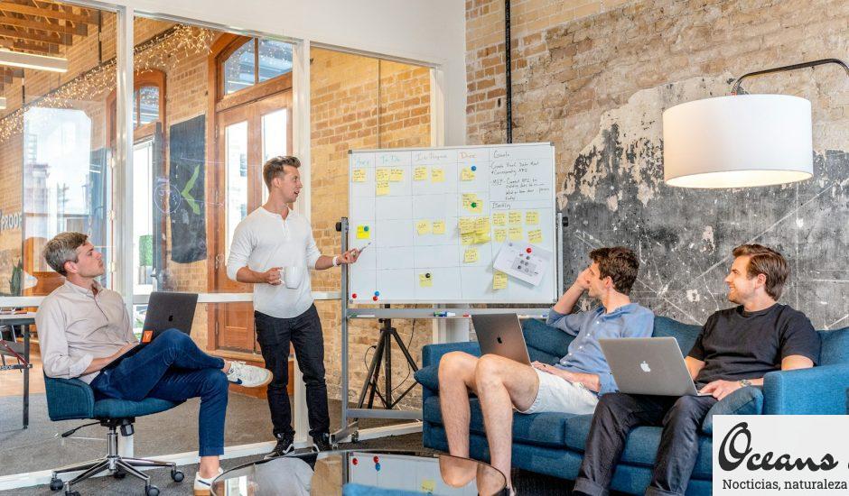 three men sitting while using laptops and watching man beside whiteboard