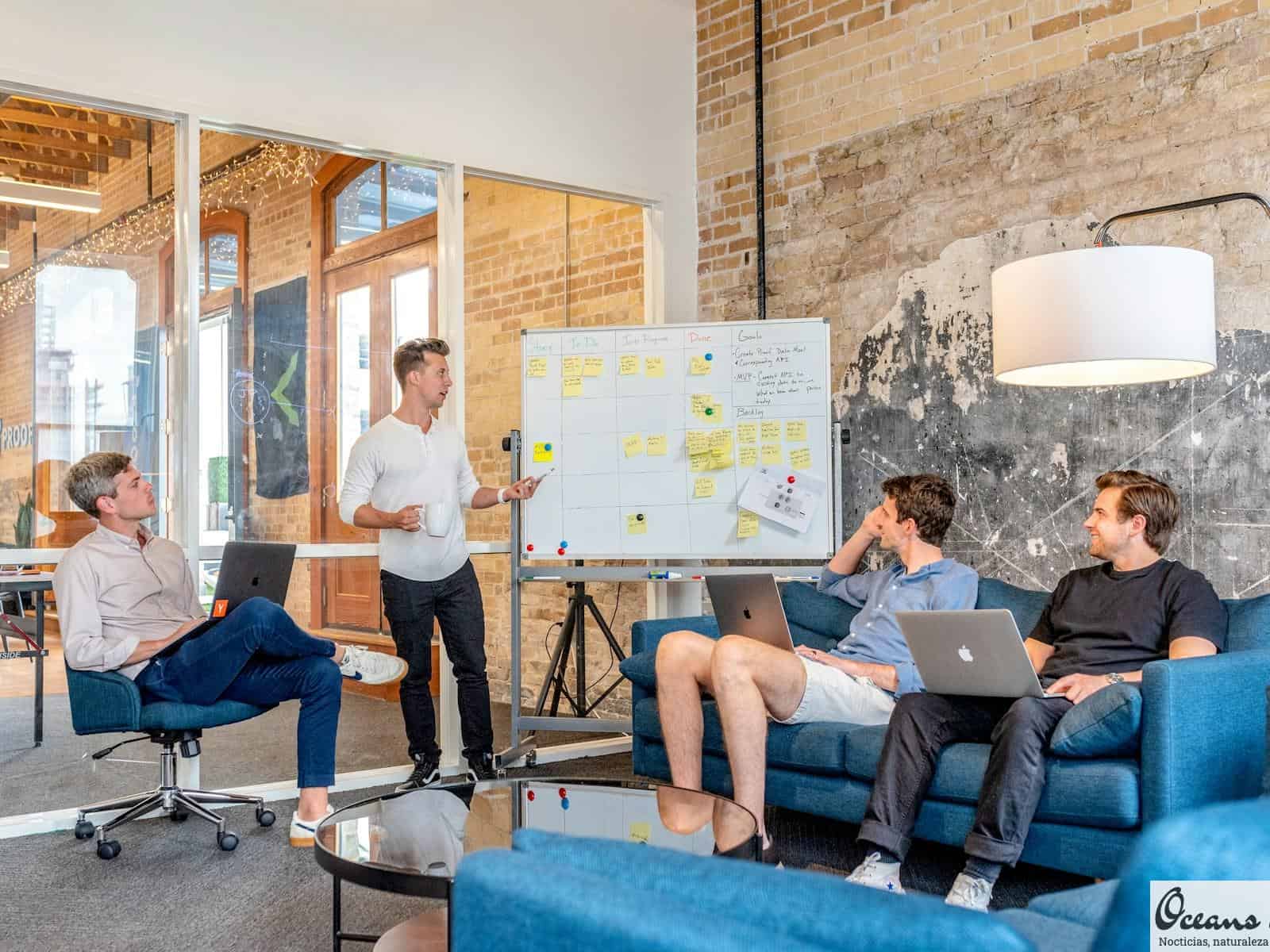 three men sitting while using laptops and watching man beside whiteboard