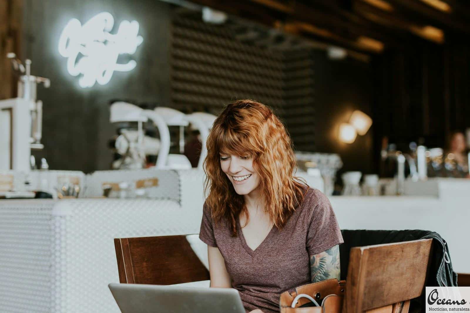 woman sitting on brown wooden chair while using silver laptop computer in room