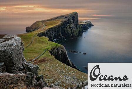 A stunning sunset view of Neist Point Lighthouse with cliffs and serene sea in Scotland.