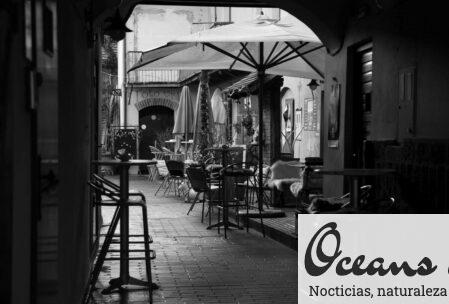 Black and white of restaurant on street with tables and chairs under umbrellas near shabby buildings in daytime in town